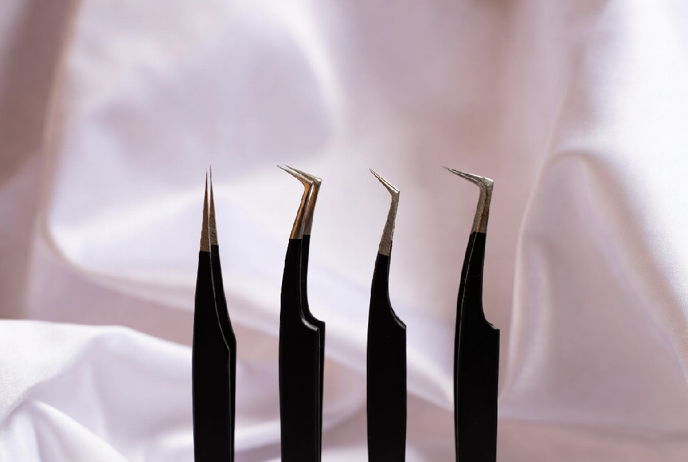 Different types of professional lash extension tweezers including straight, curved, volume and isolation tweezers laid out on white background
