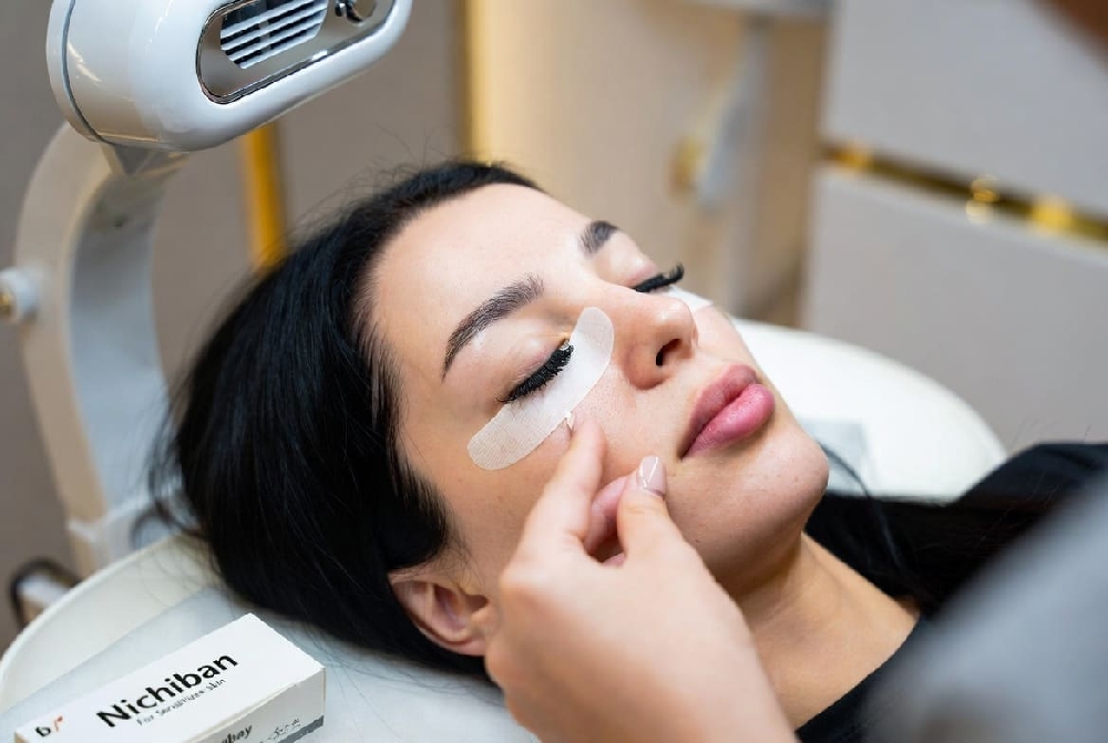 Professional lash artist applying gentle Japanese Nichiban tape to secure lower lashes during eyelash extensions in a Dubai salon, ensuring comfort for sensitive skin