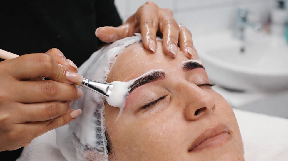 Esthetician applying clinical foam cleanser with brush for deep brow skin prep before tinting